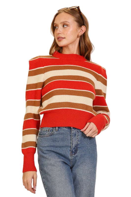 Woman wearing a red, brown, and beige striped sweater with blue jeans on 