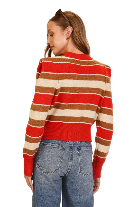 Woman wearing a red, brown, and beige striped sweater with blue jeans on.  Back view of sweater. 