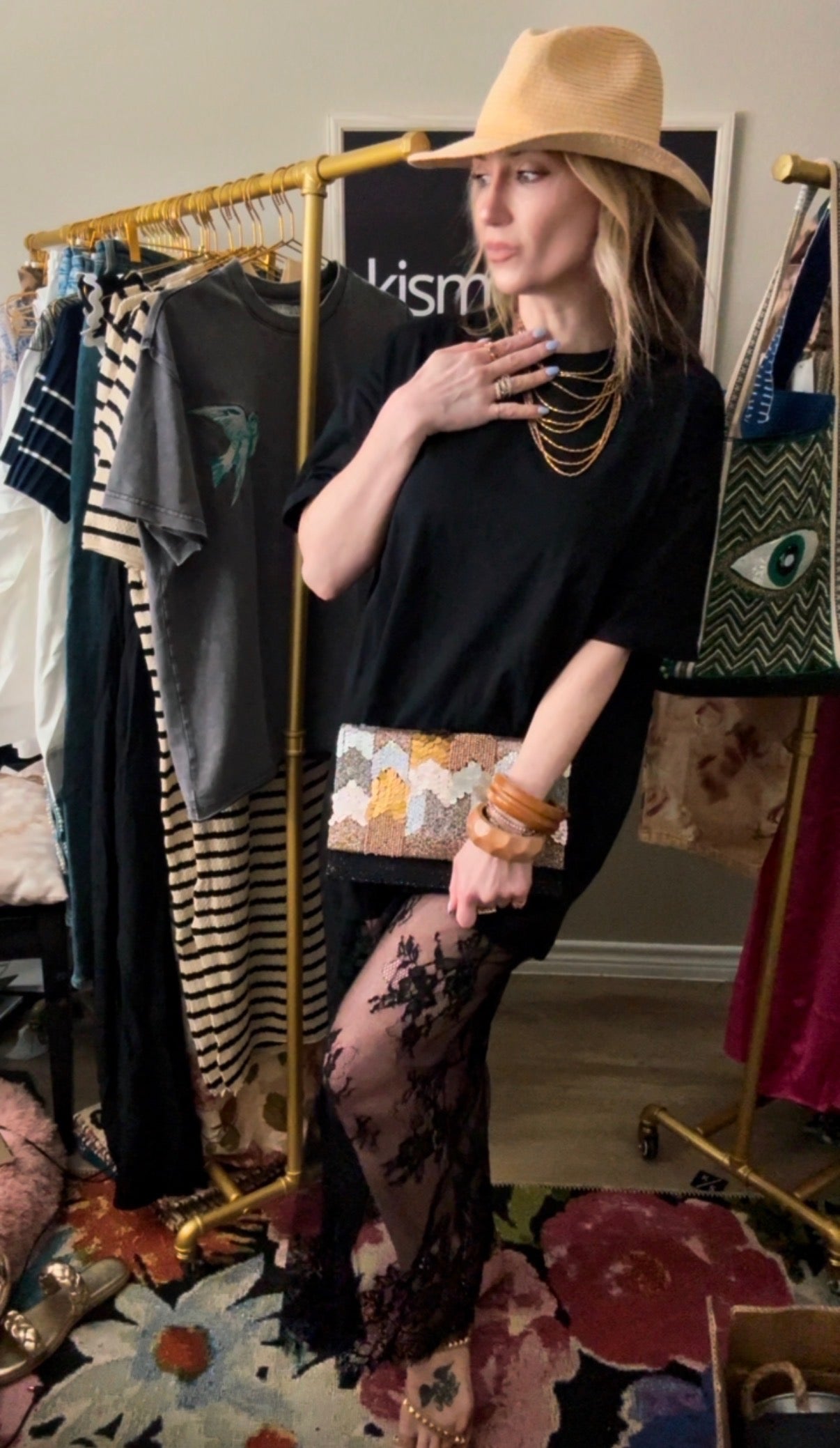 Woman in a stylish outfit with a hat and clutch in a room with clothing racks.