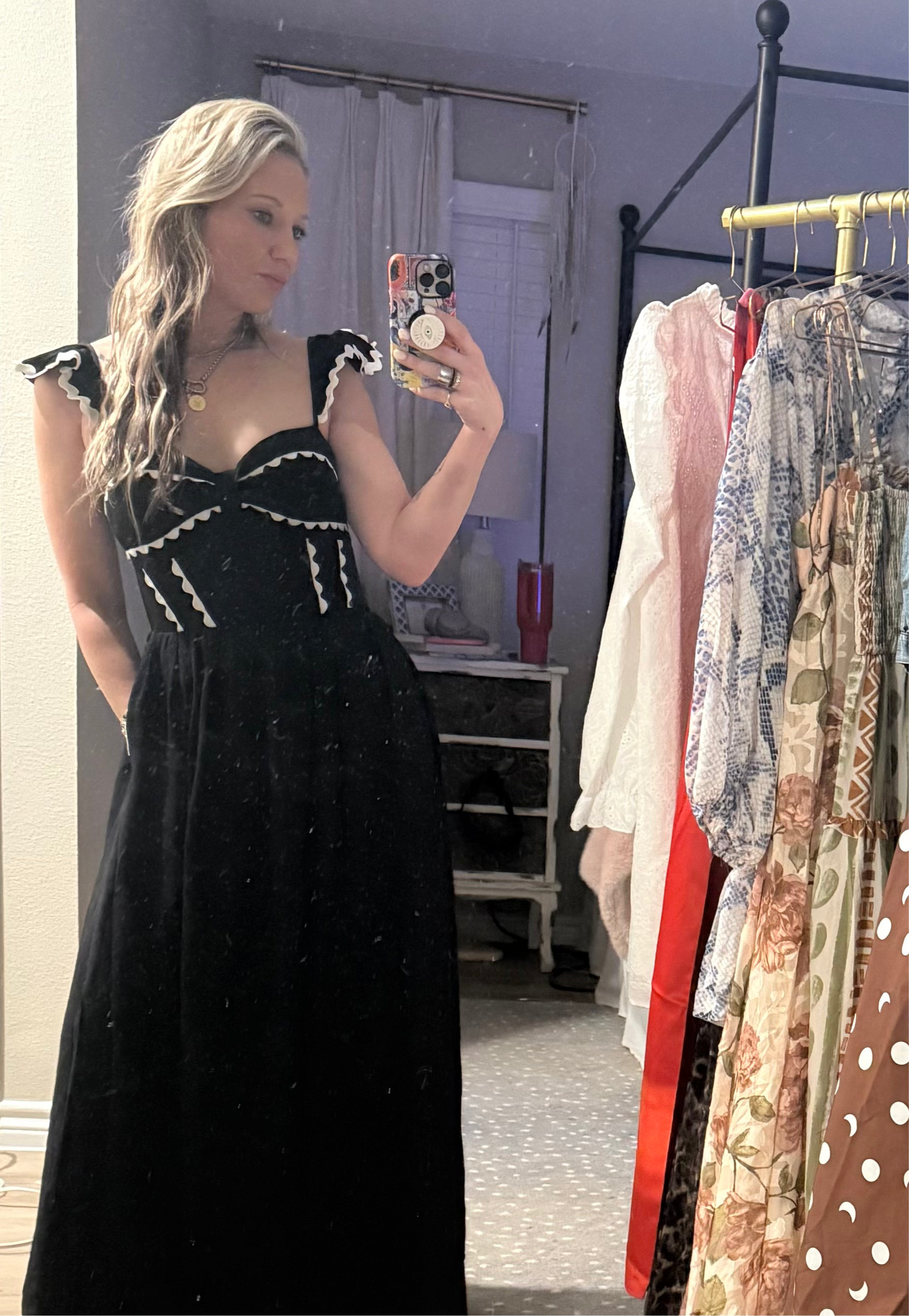 Woman wearing a black dress with white trim in a room with clothing racks.