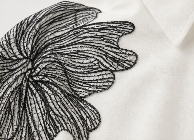 Detailed view of white blouse with black floral embroidery on a white background
